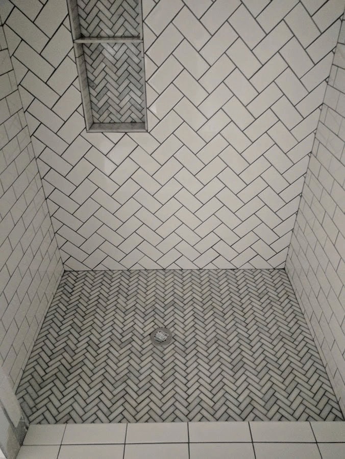 Shower tile ideas with white subway tile in herringbone pattern, dark grout and coordinating mosaic shower floor