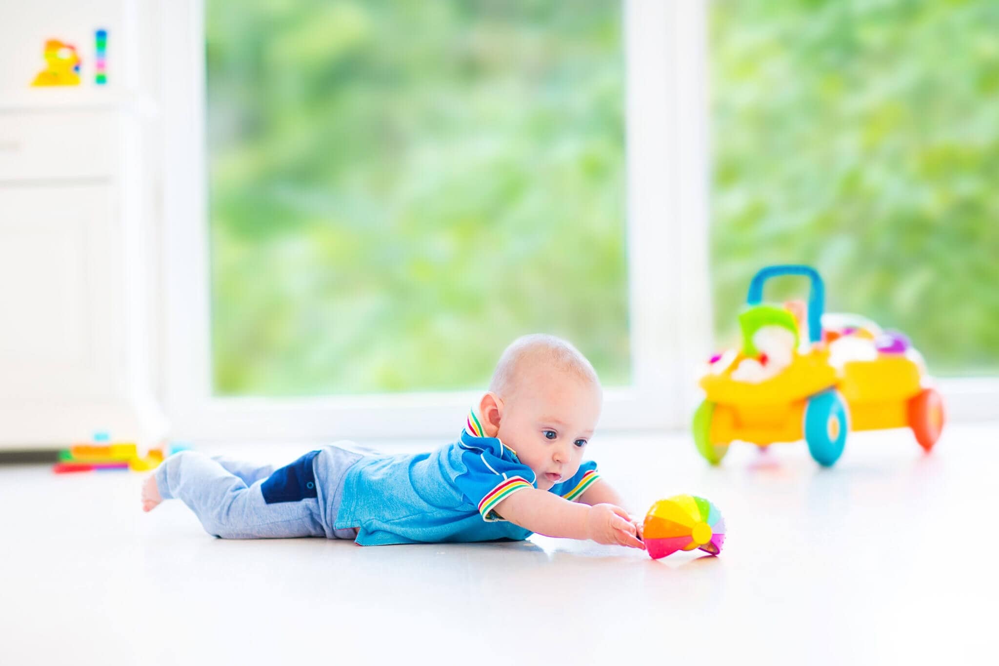 A baby boy lies on his stomach on the floor and plays with a toy
