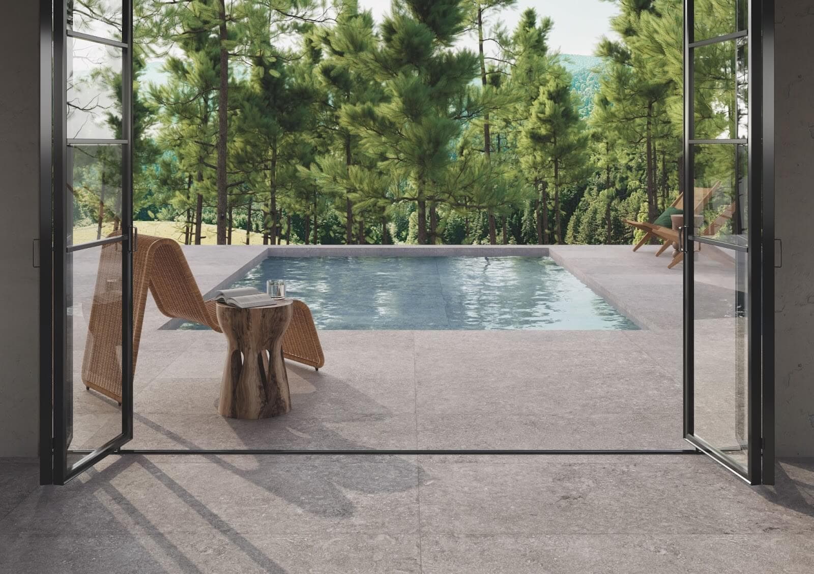 View of an outdoor residential pool with a lounge chair and side table beside it, surrounded by gray stone look tile with pine trees in the foreground.
