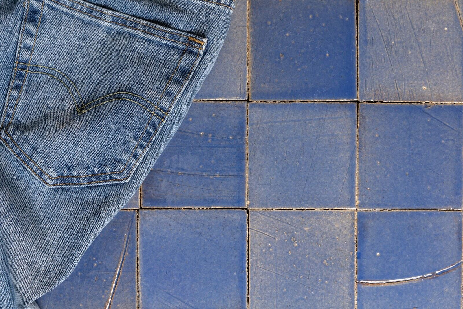 Denim jeans placed atop different tones of blue tiles