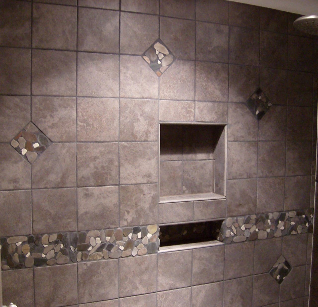 Stacked shower niches with rustic stone-look tile, mosaic stripe, and diamond insets in ivory, pastel yellow, and pink