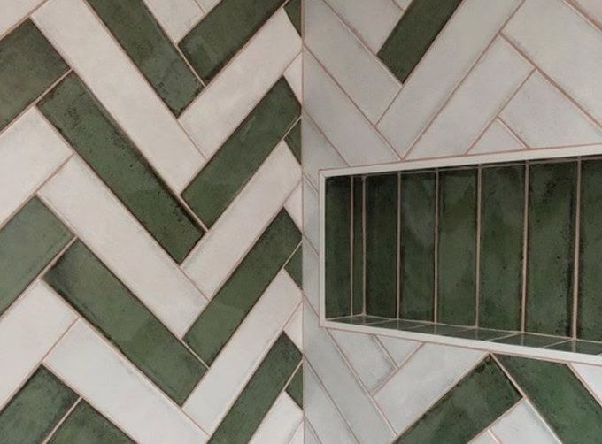 Variegated green tile in a single row lines this horizontal shower niche, while herringbone green-and-white tile walls