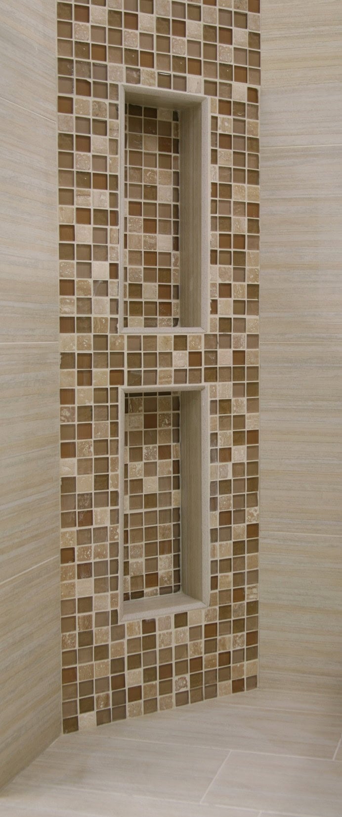 Tile corner shower niche with mosaic tile in natural hues framed by stone-look tile that subtly contrasts with the matching walls and floor