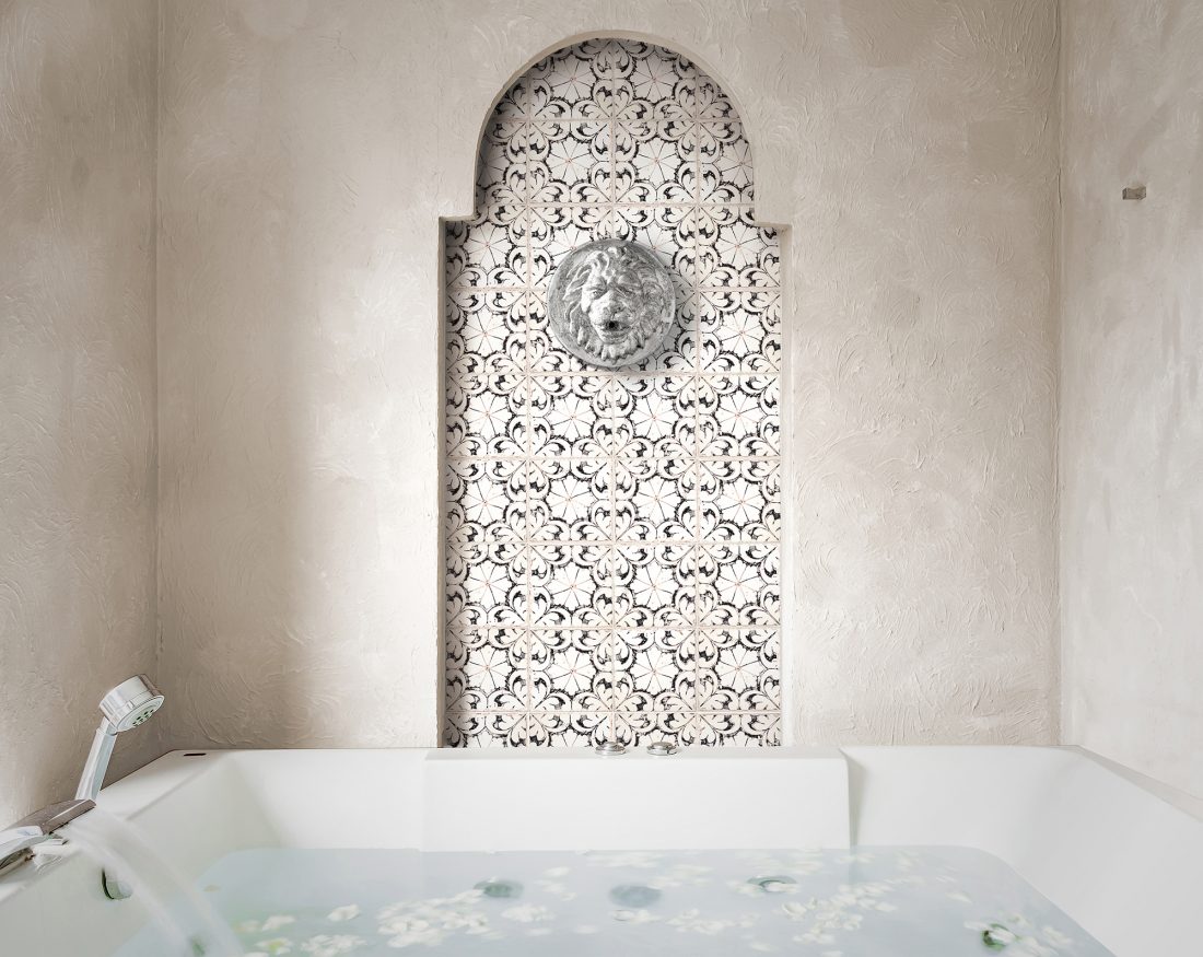 Floral-patterned black, white, and cream tile serves as the focal point, with a luxurious arched niche and lion’s-head spout in this spa-like bathroom