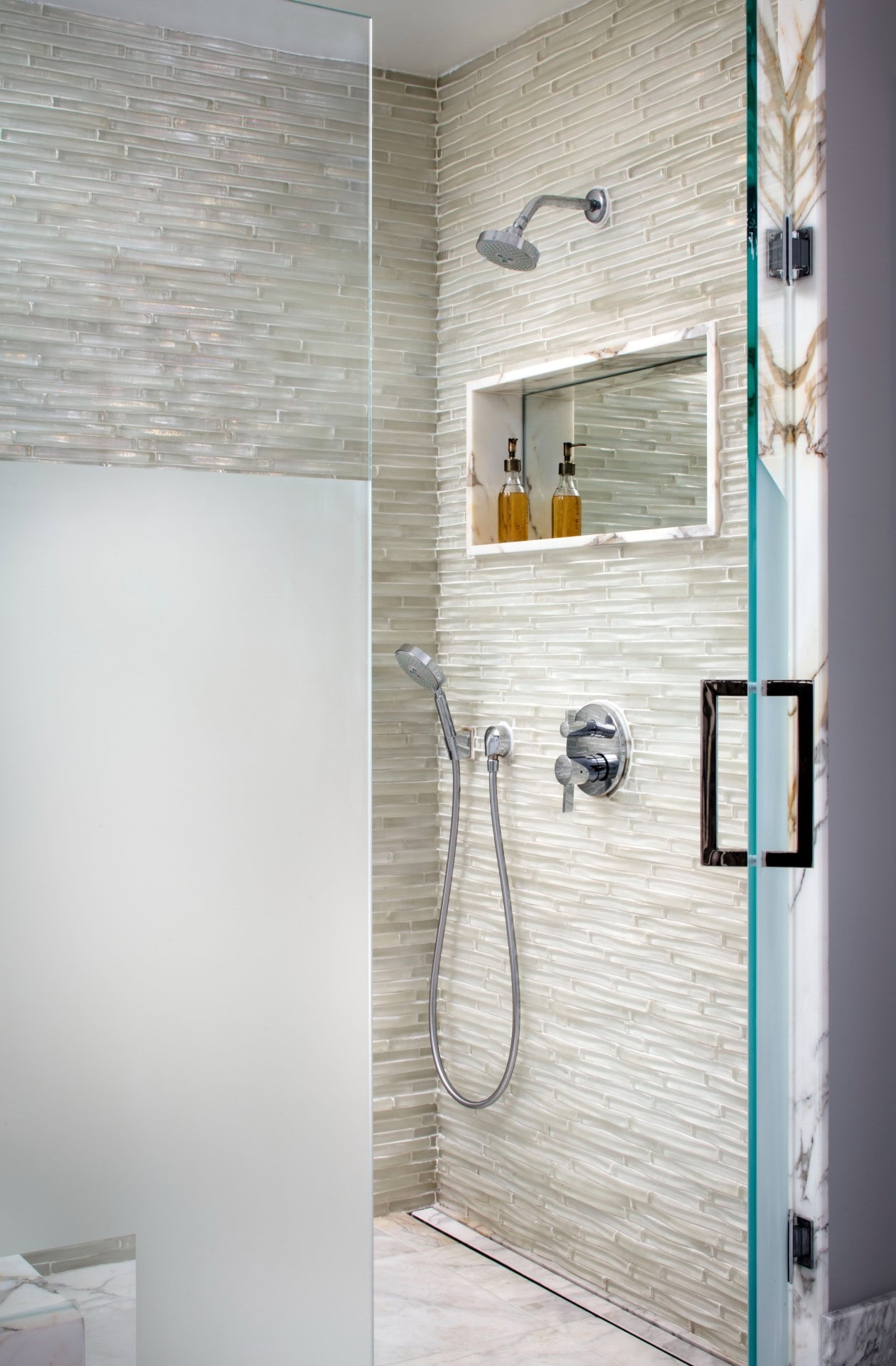 Creamy marble-look tile frames the sides of this shower niche, hosting self-care practicality with a back panel mirror