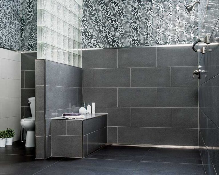 Small corner shower with built-in bench clad in slate-gray and black-and-white mosaic tiles