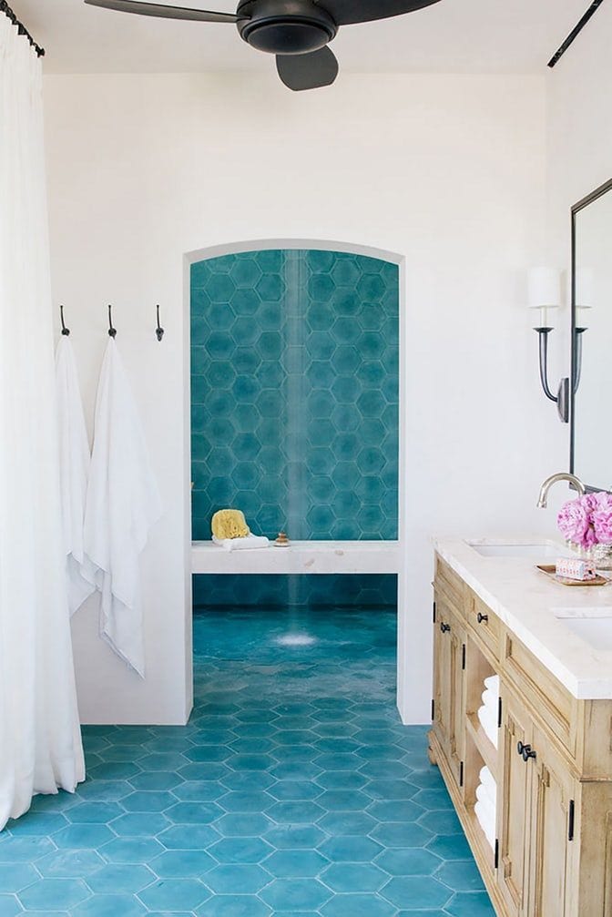 Shower interior with a white marble-look floating bench and teal hexagon tile walls