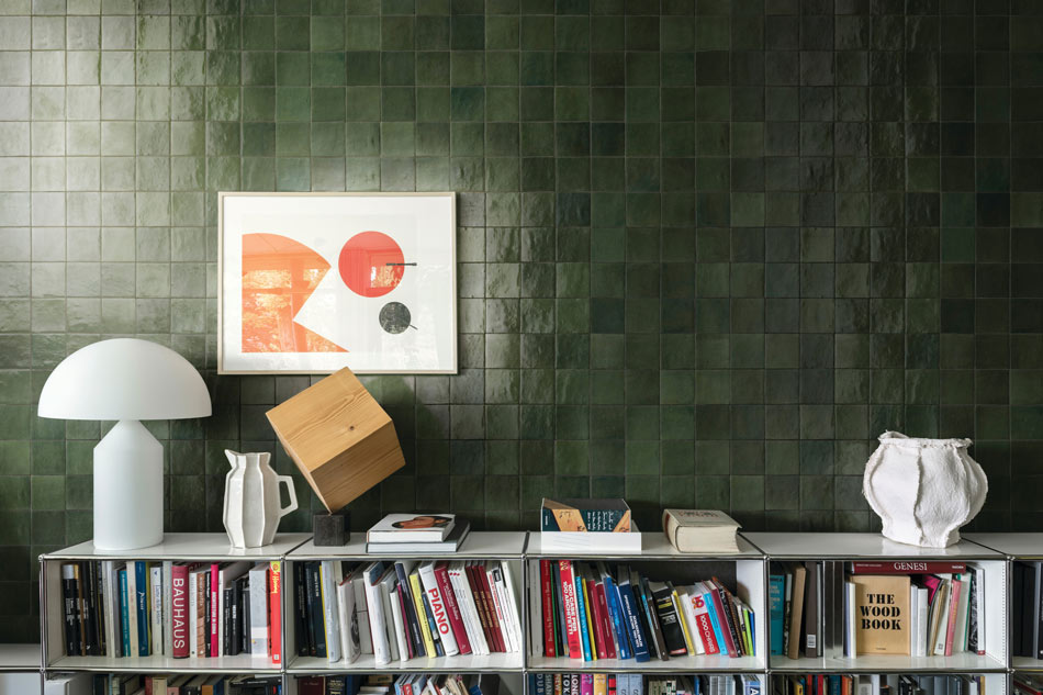 Interior wall of dark forest-green square tiles above a bookshelf filled with books