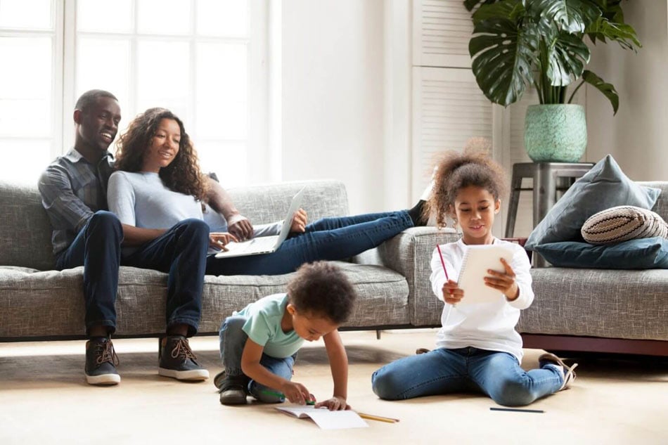 Family relaxing and children drawing on XXL creamy neutral ceramic tile floor panels in a living room that doubles as a playroom