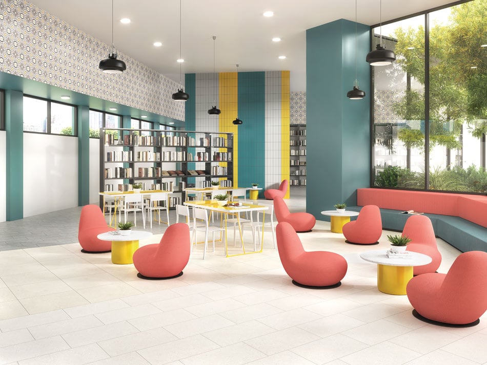 Children’s library with ivory floor tile, teal and yellow vertical accent wall panels, wallpaper-look tile motifs on high ceilings, and playful flamingo-pink seating