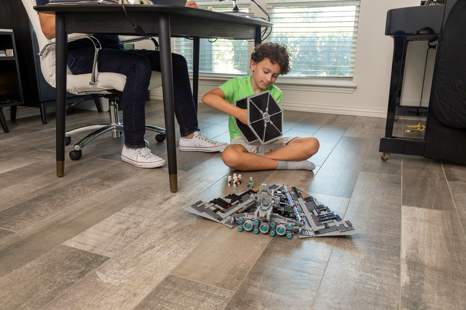 Child playing with toy spaceships on rustic wood-look ceramic tile flooring in a shared family room