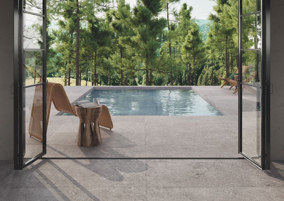 Outdoor pool area with weathered stone-look porcelain tile slabs creating a seamless indoor-outdoor transition