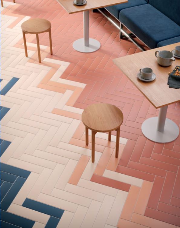 Cafeteria floor with color-blocked herringbone tile in terracotta, peach, white, and denim-blue tones