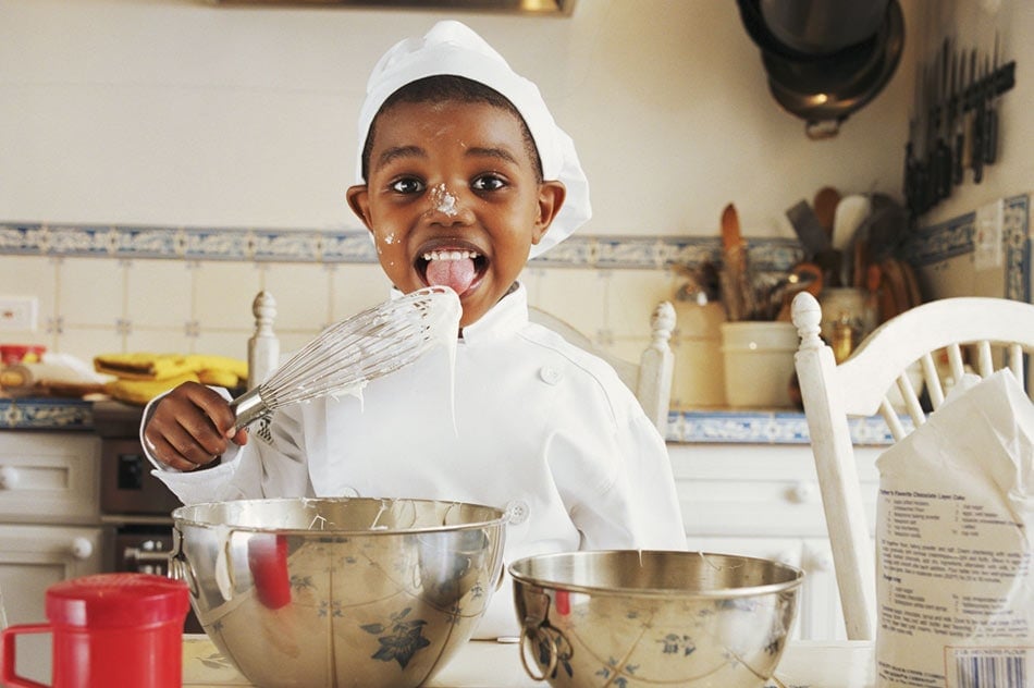 Smiling child in chef outfit cooking in a kitchen with ceramic tile countertops and patterned tile backsplash