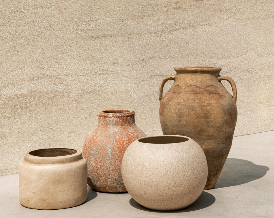 Collection of rustic clay pots displayed against a textured, warm-toned ceramic tile wall